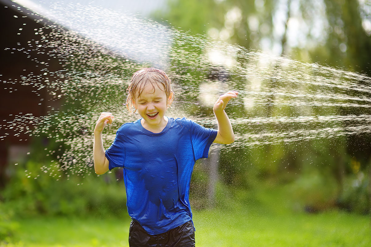 boy running through sprinkler in hot weather