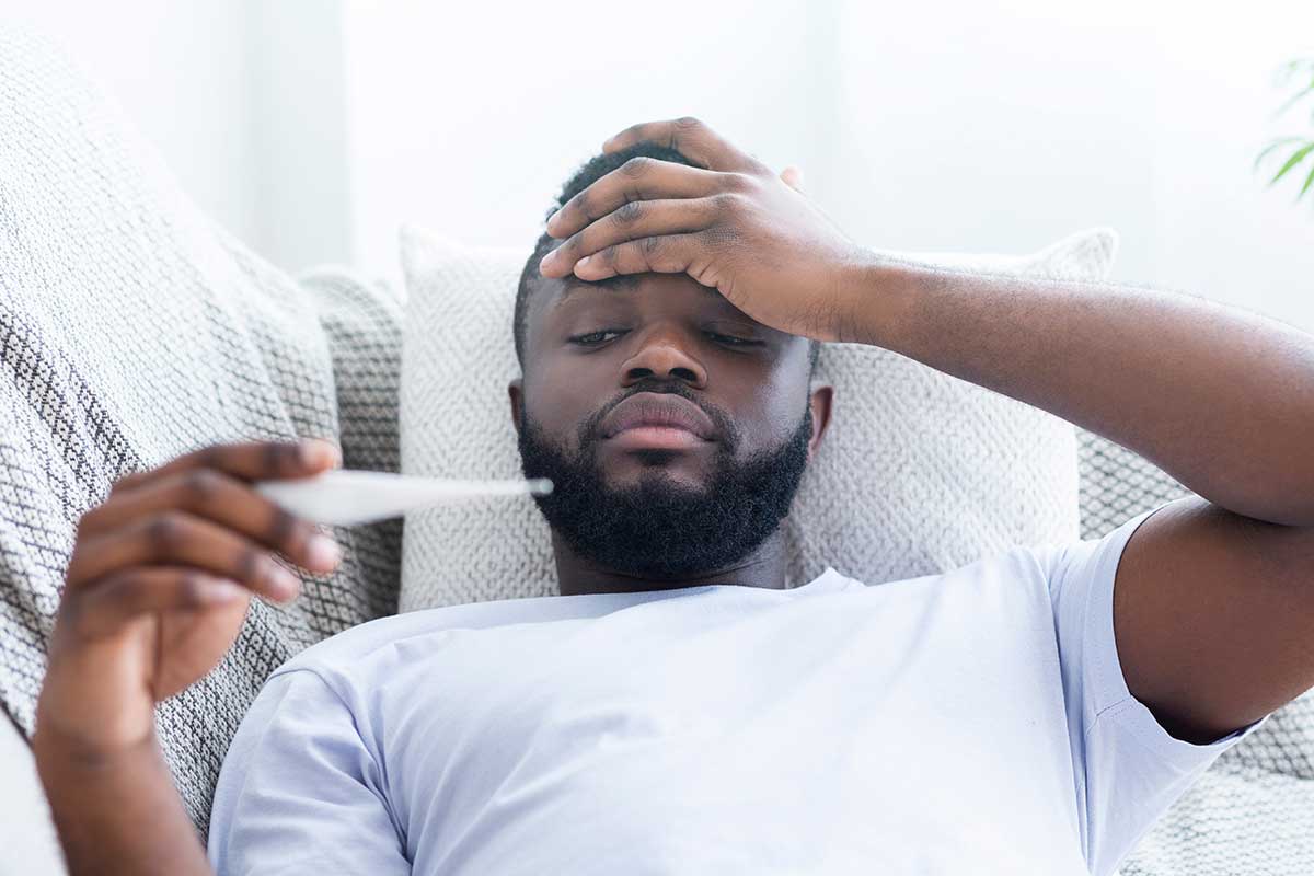 sick man in bed with the flu holding a thermometer