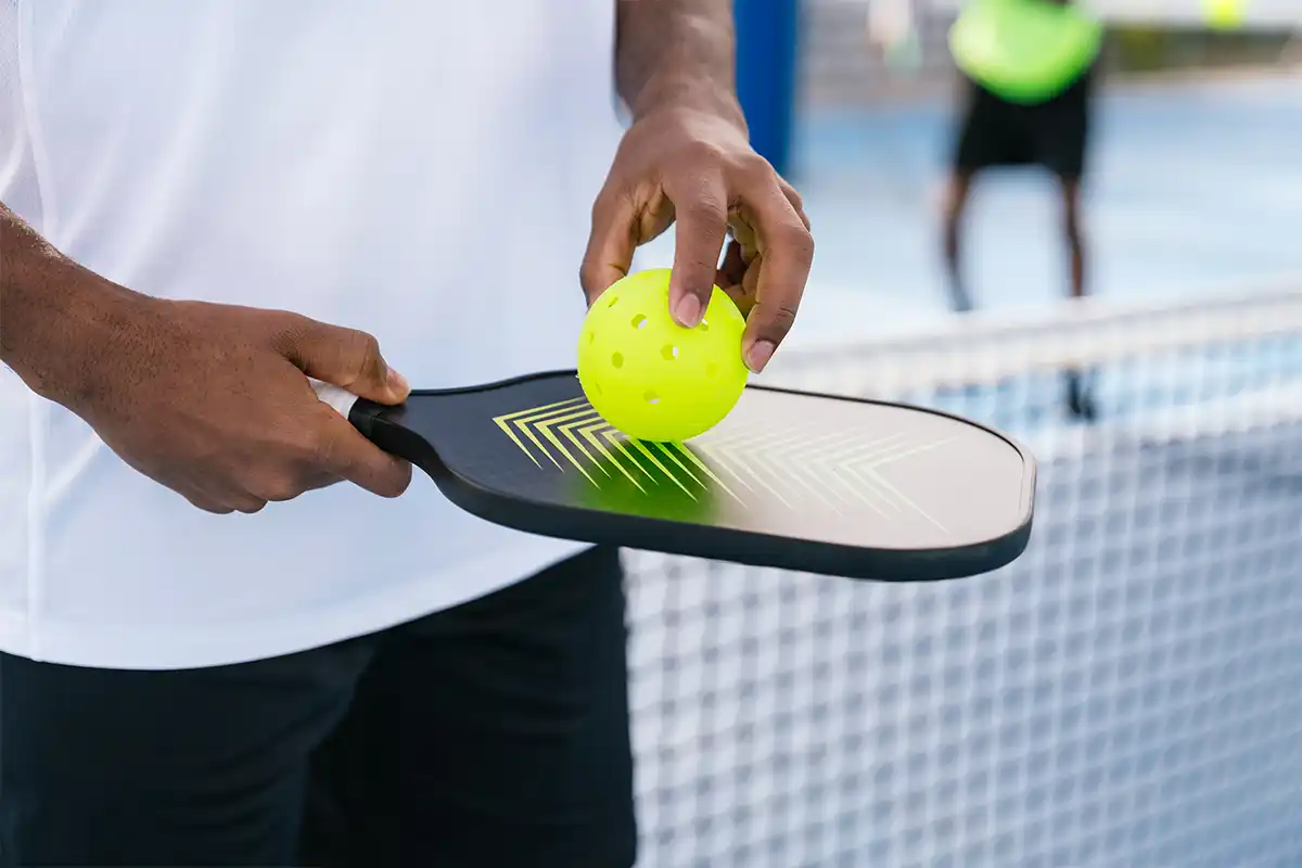 person holding pickleball and paddle